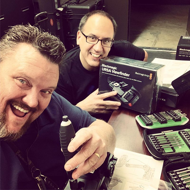 Two men smiling and holding video equipment.